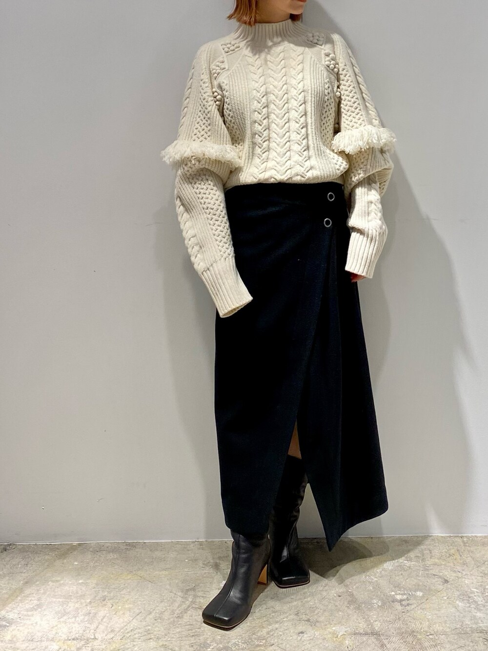 ブラック系のスカート、ブラック系のブーツ、ホワイト系のニット/セーターを着用したレディースの春コーディネートの3枚目の写真