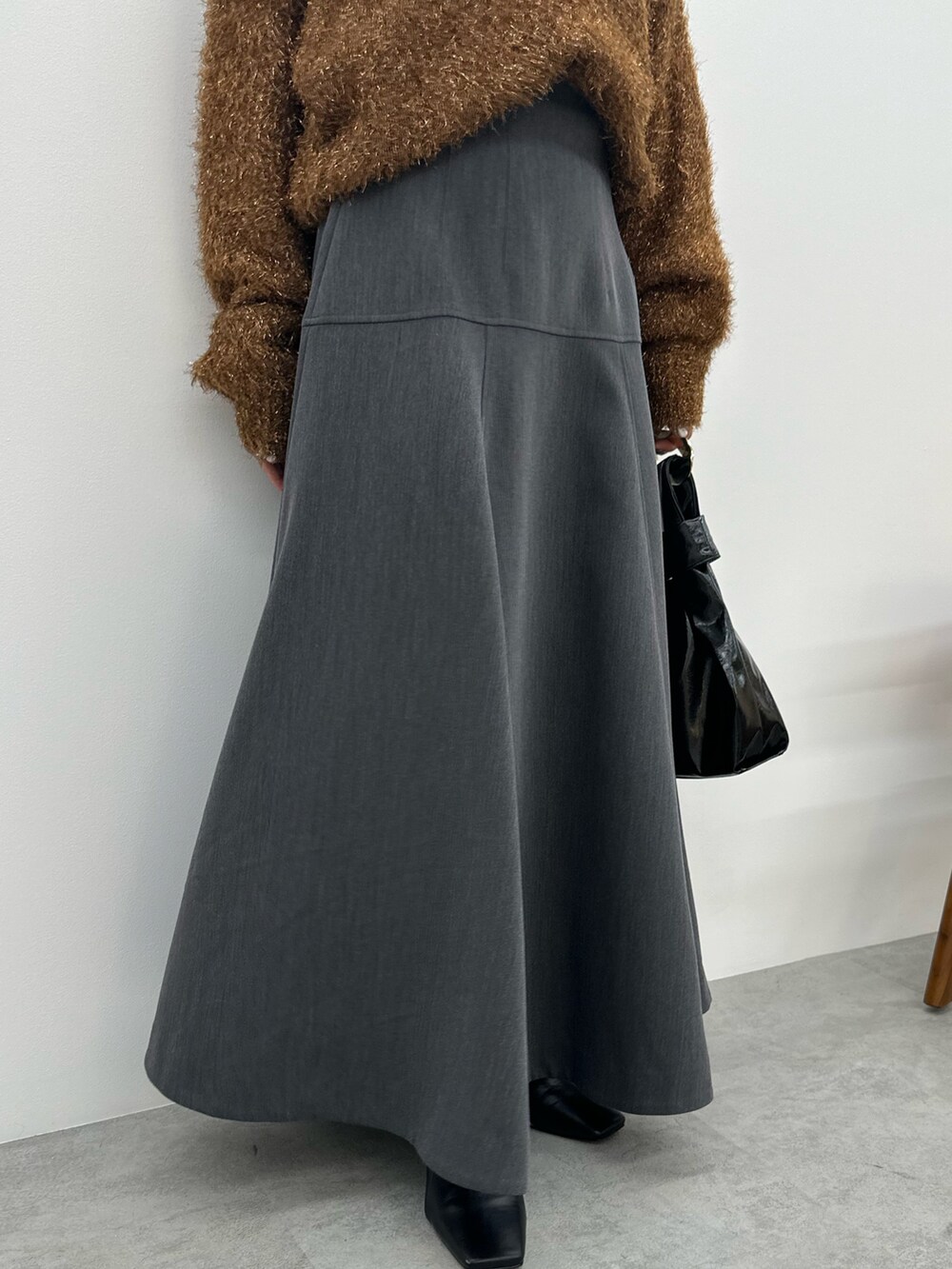 オレンジ系のニット/セーター、グレー系のスカート、ブラック系のブーツを着用したレディースの秋コーディネートの8枚目の写真