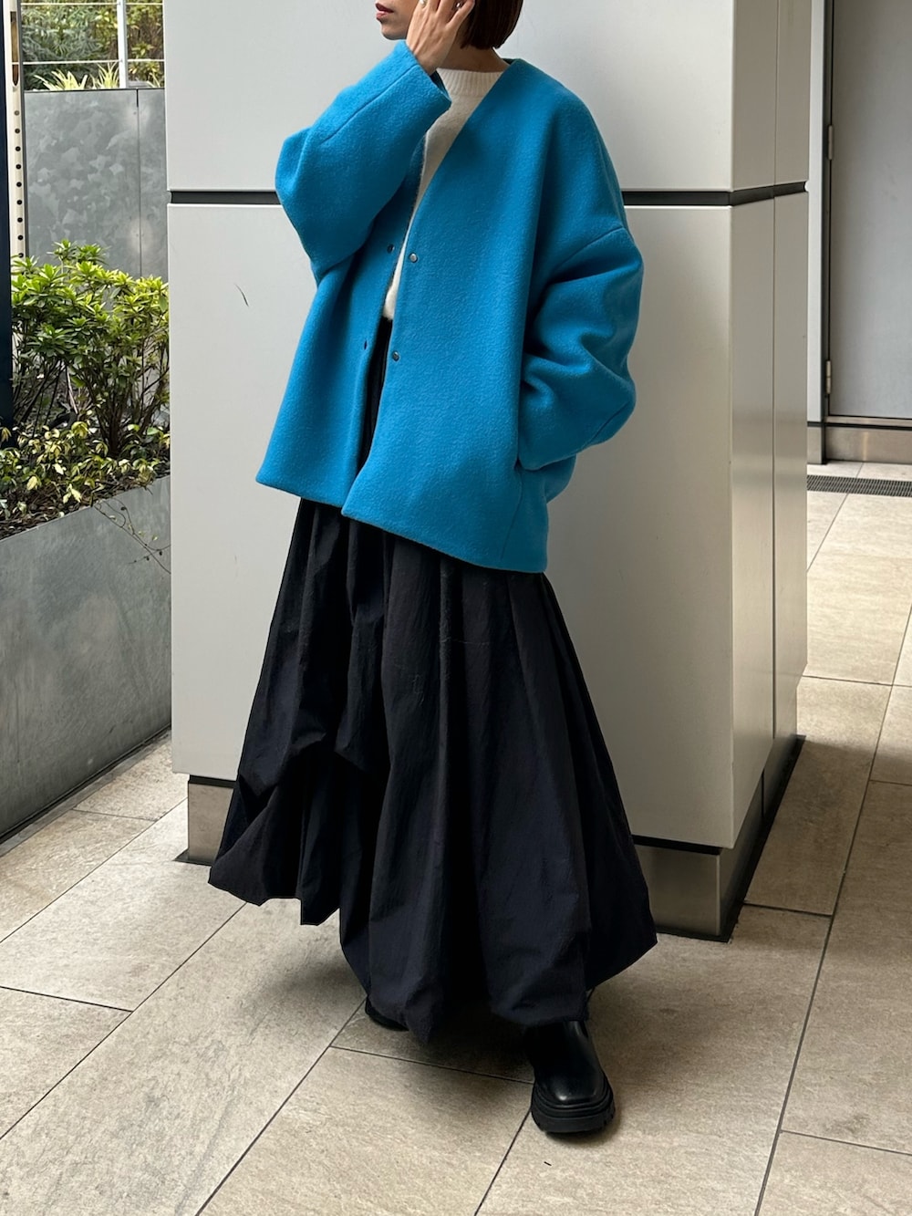 ブルー系のノーカラーコート、ブラック系のスカート、ホワイト系のニット/セーターを着用したレディースの冬コーディネートの2枚目の写真