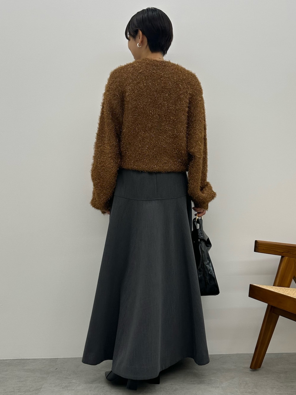 オレンジ系のニット/セーター、グレー系のスカート、ブラック系のブーツを着用したレディースの秋コーディネートの4枚目の写真