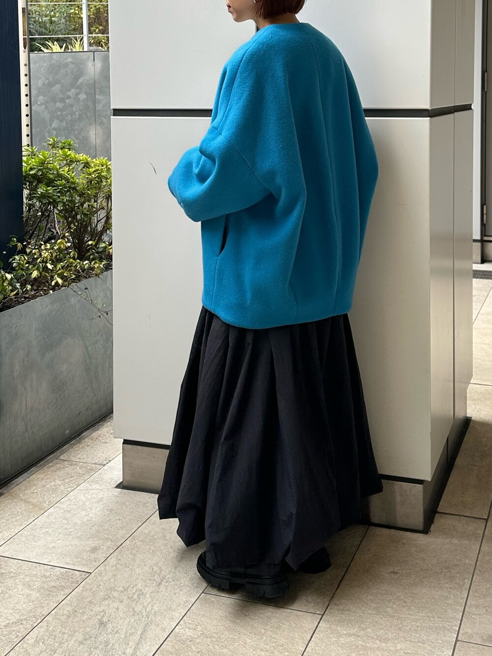 ブルー系のノーカラーコート、ブラック系のスカート、ホワイト系のニット/セーターを着用したレディースの冬コーディネートの4枚目の写真