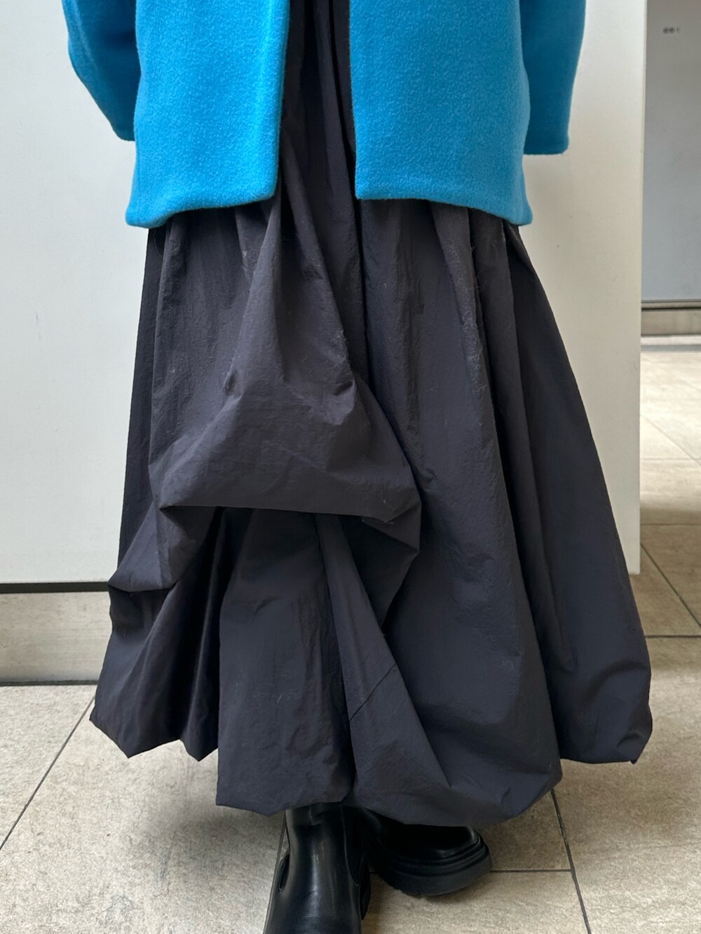 ブルー系のノーカラーコート、ブラック系のスカート、ホワイト系のニット/セーターを着用したレディースの冬コーディネートの7枚目の写真