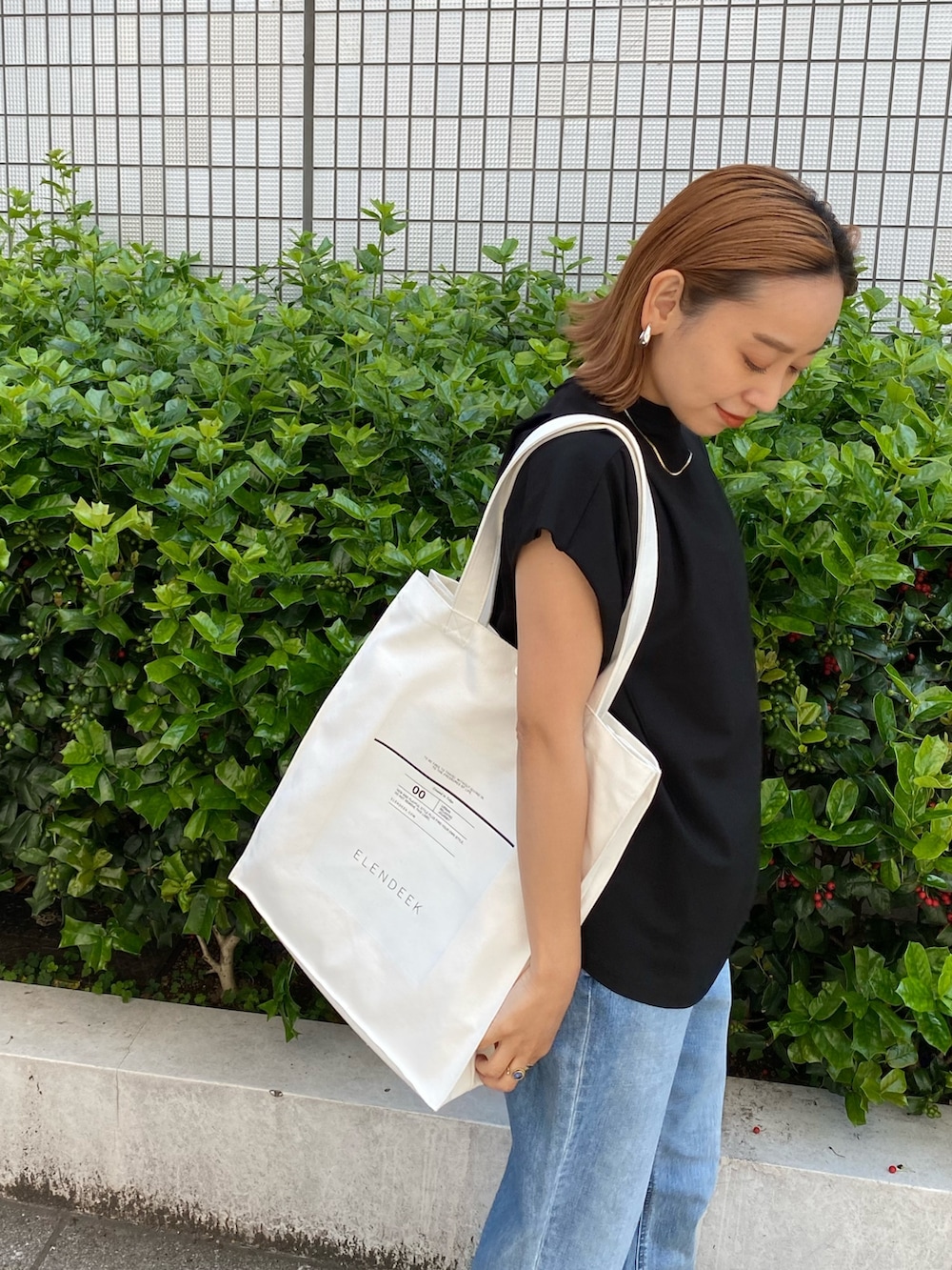 ホワイト系のトートバッグ、ブラック系のTシャツ/カットソー、ブルー系のデニムパンツを着用したレディースの春コーディネートの4枚目の写真