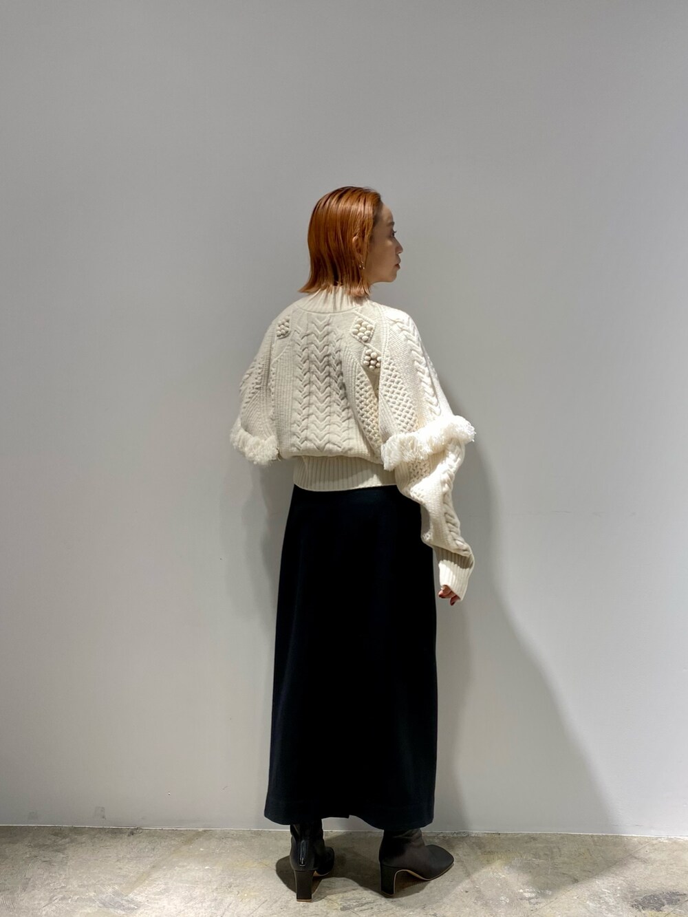ブラック系のスカート、ブラック系のブーツ、ホワイト系のニット/セーターを着用したレディースの春コーディネートの6枚目の写真