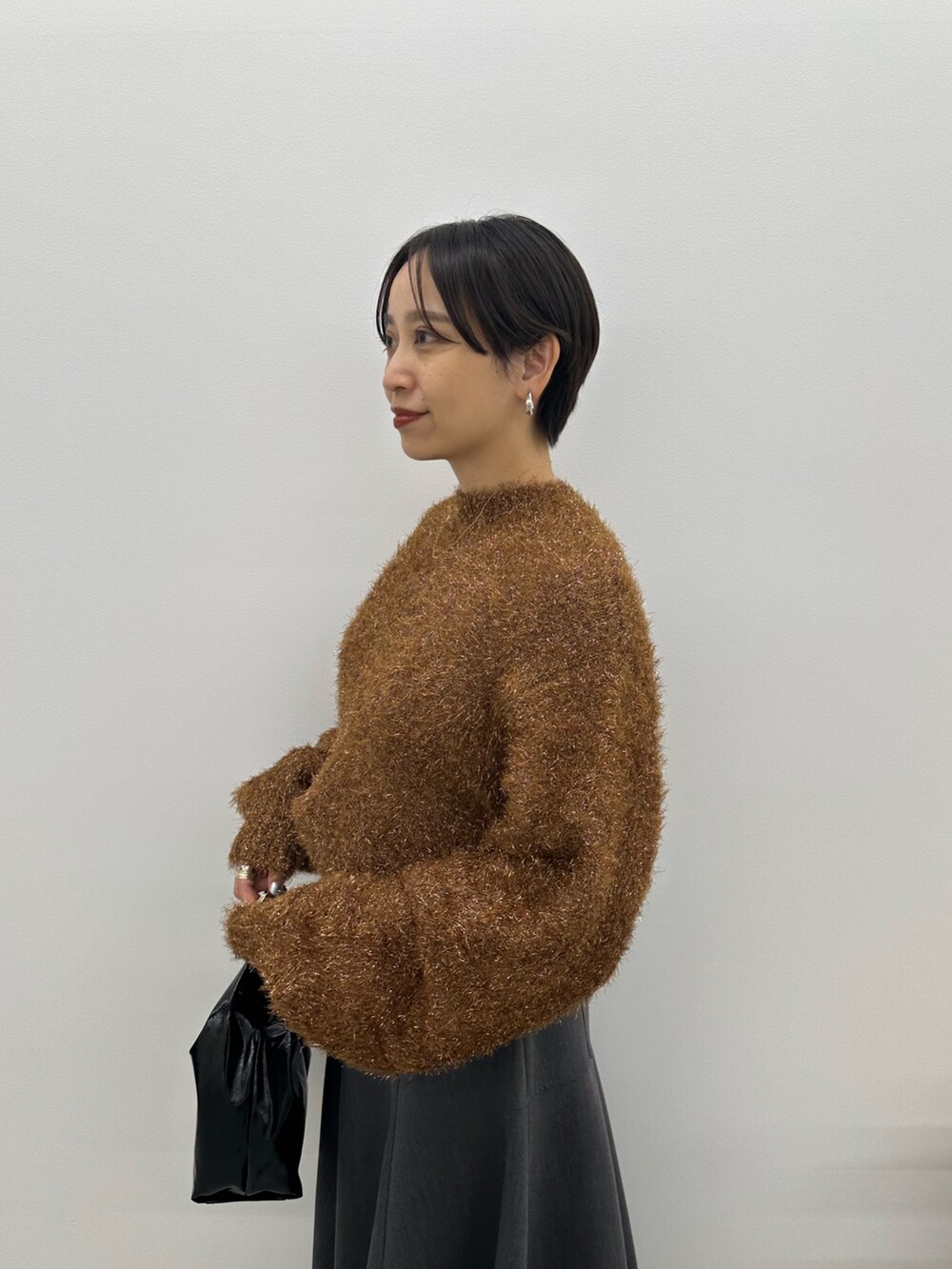 オレンジ系のニット/セーター、グレー系のスカート、ブラック系のブーツを着用したレディースの秋コーディネートの5枚目の写真