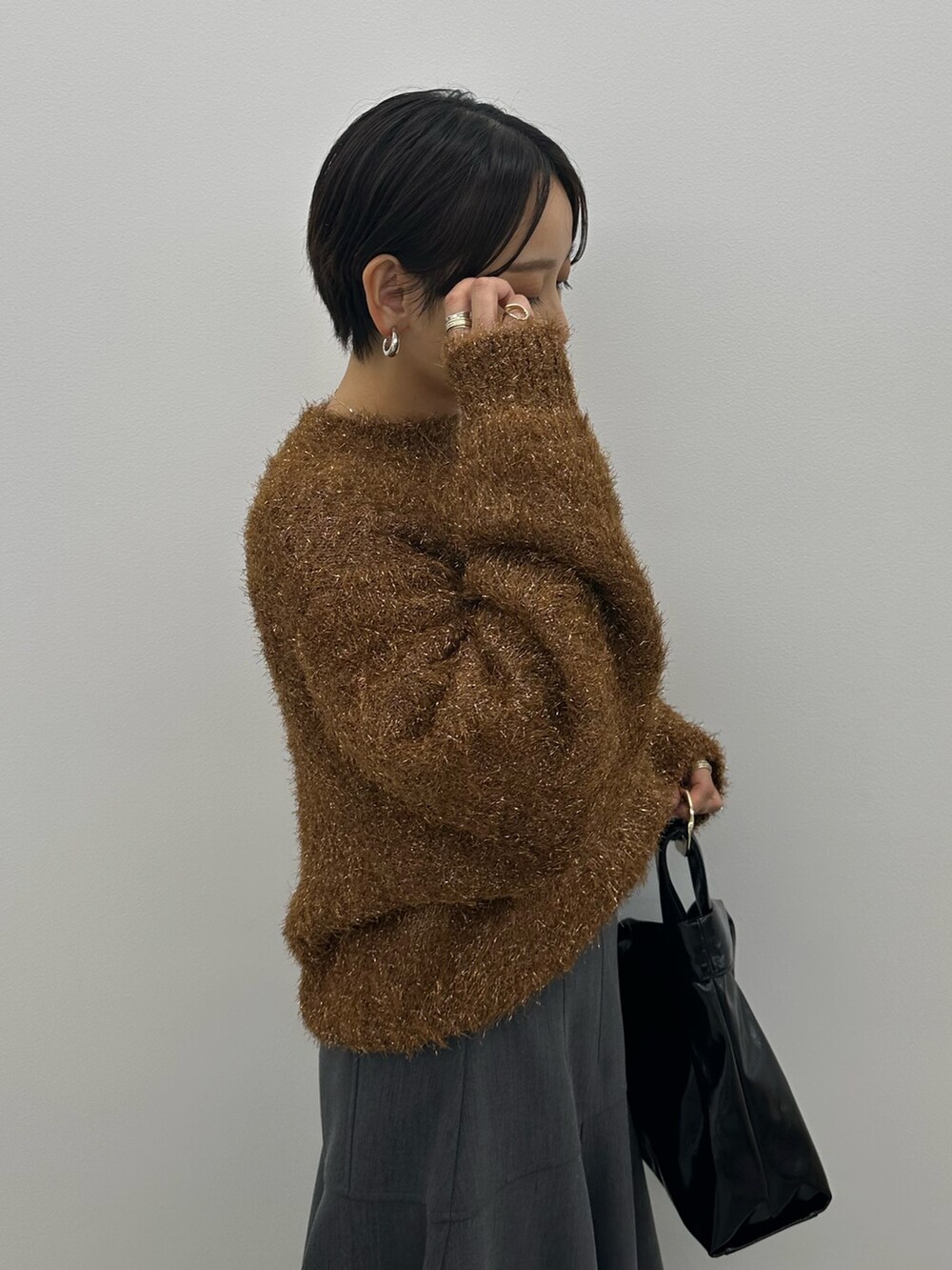 オレンジ系のニット/セーター、グレー系のスカート、ブラック系のブーツを着用したレディースの秋コーディネートの7枚目の写真