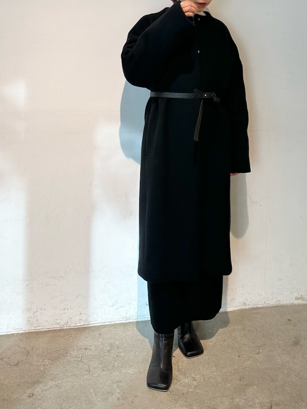 ブラック系のノーカラーコート、ブラック系のブーツ、ホワイト系のニット/セーターを着用したレディースの秋コーディネートの5枚目の写真