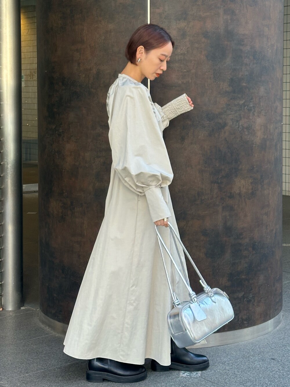 シルバー系のボストンバッグ、ブラック系のブーツ、ベージュ系のワンピースを着用したレディースの冬コーディネートの4枚目の写真