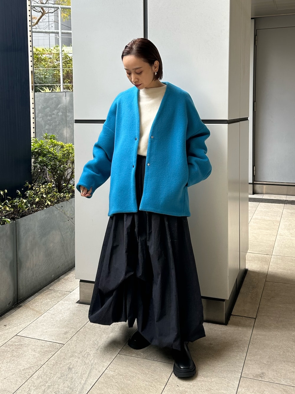 ブルー系のノーカラーコート、ブラック系のスカート、ホワイト系のニット/セーターを着用したレディースの冬コーディネートの3枚目の写真