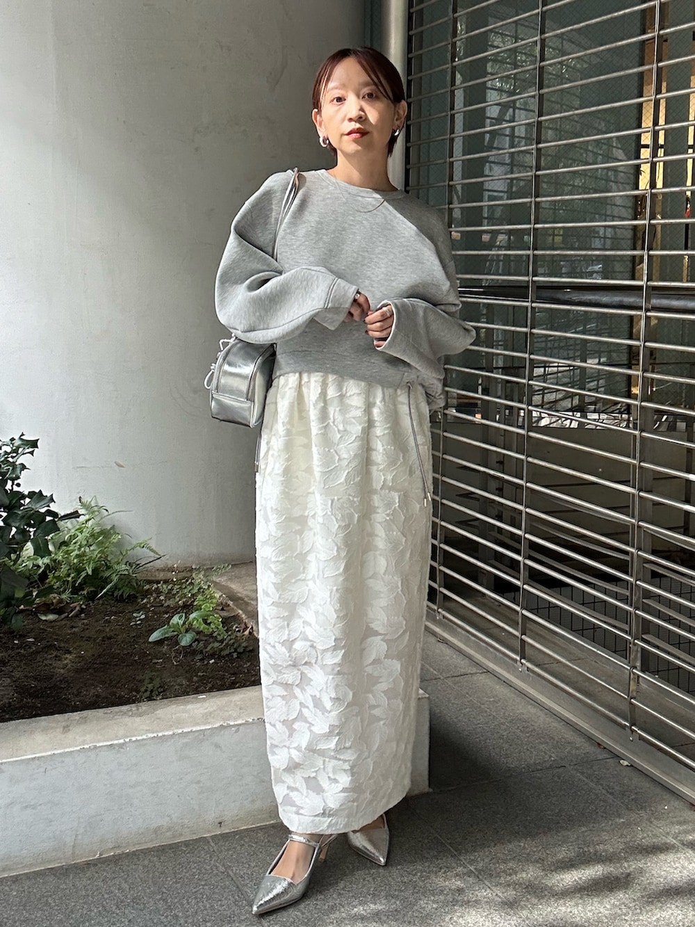 グレー系のスウェット、ホワイト系のスカート、シルバー系のボストンバッグを着用したレディースの冬コーディネートの2枚目の写真