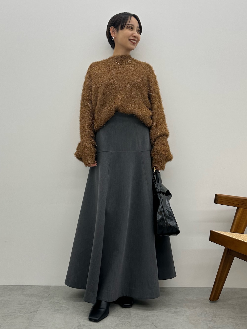 オレンジ系のニット/セーター、グレー系のスカート、ブラック系のブーツを着用したレディースの秋コーディネートの2枚目の写真