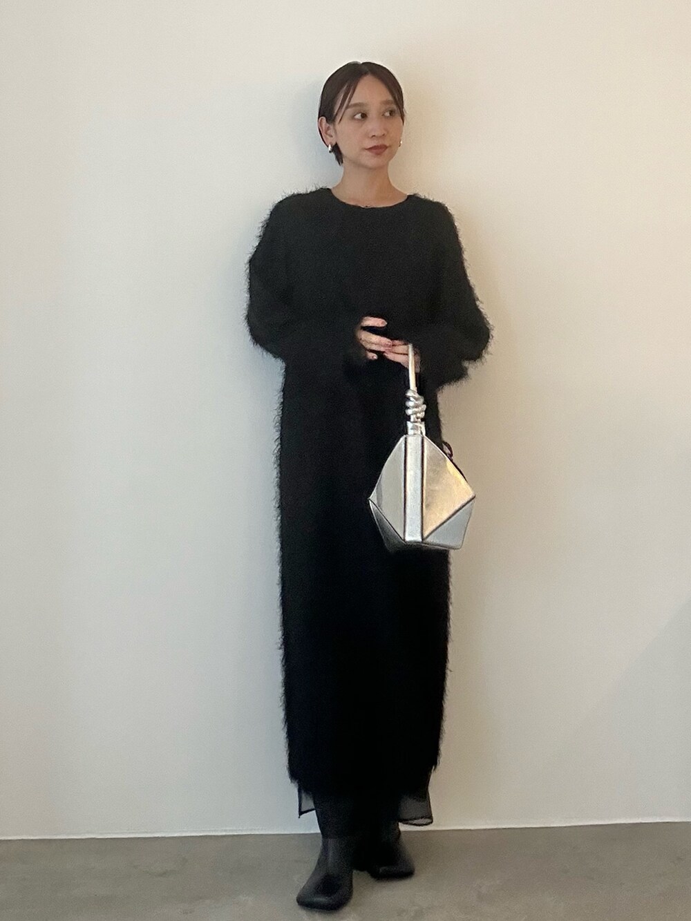 ブラック系のワンピース、シルバー系のハンドバッグ、ブラック系のブーツを着用したレディースの秋コーディネートの2枚目の写真