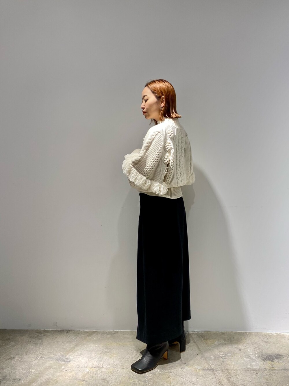 ブラック系のスカート、ブラック系のブーツ、ホワイト系のニット/セーターを着用したレディースの春コーディネートの4枚目の写真