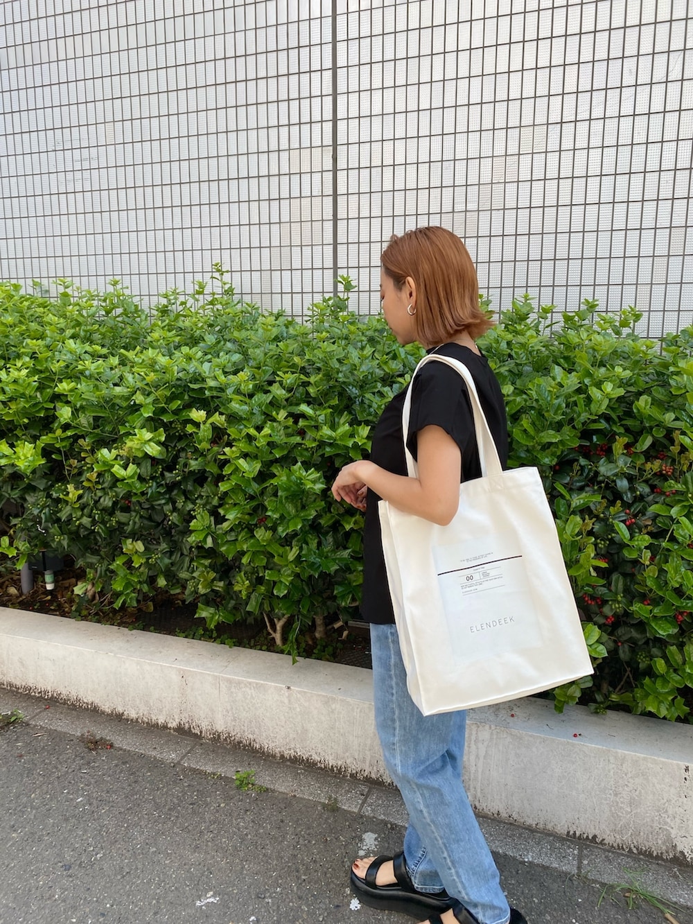 ホワイト系のトートバッグ、ブラック系のTシャツ/カットソー、ブルー系のデニムパンツを着用したレディースの春コーディネートの3枚目の写真