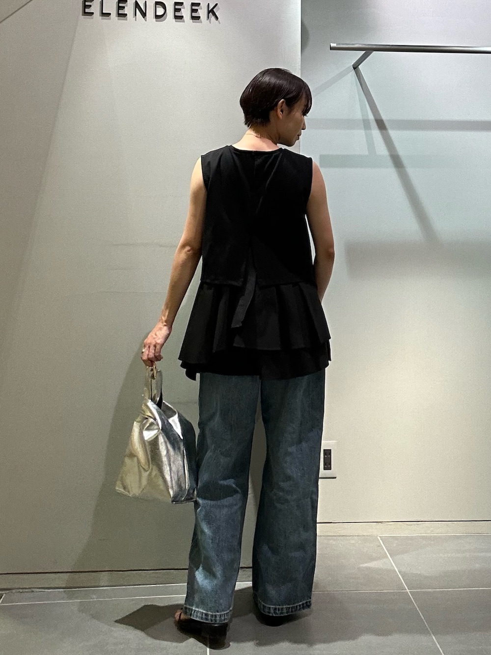 ブルー系のデニムパンツ、シルバー系のハンドバッグ、ブラック系のタンクトップを着用したレディースの夏コーディネートの4枚目の写真
