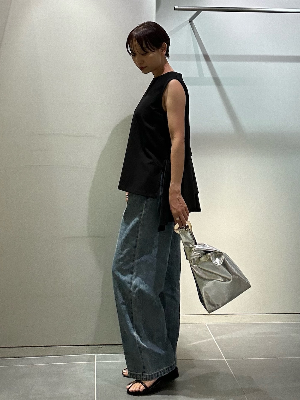 ブルー系のデニムパンツ、シルバー系のハンドバッグ、ブラック系のタンクトップを着用したレディースの夏コーディネートの3枚目の写真