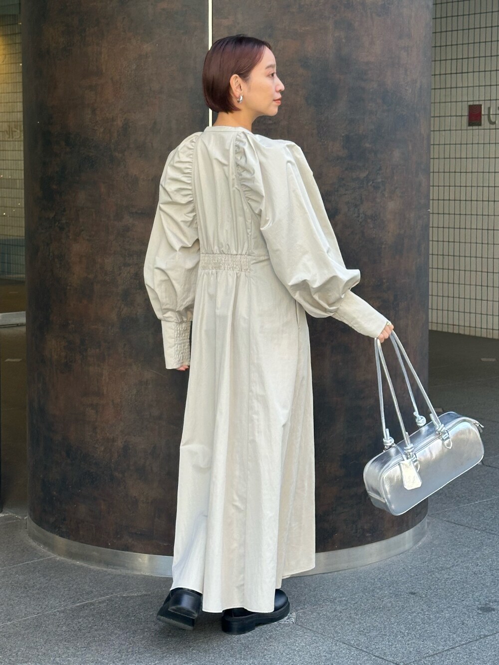 シルバー系のボストンバッグ、ブラック系のブーツ、ベージュ系のワンピースを着用したレディースの冬コーディネートの3枚目の写真