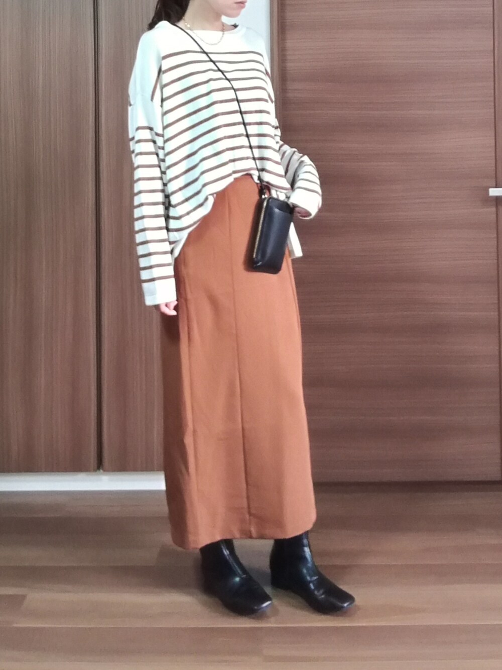オレンジ系のスカート、ブラック系のショルダーバッグ、ブラック系のブーツを着用したレディースの秋コーディネートの2枚目の写真