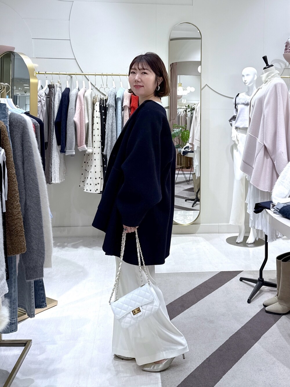 ブルー系のノーカラーコート、グリーン系のニット/セーター、ホワイト系のスラックスを着用したレディースの冬コーディネートの2枚目の写真