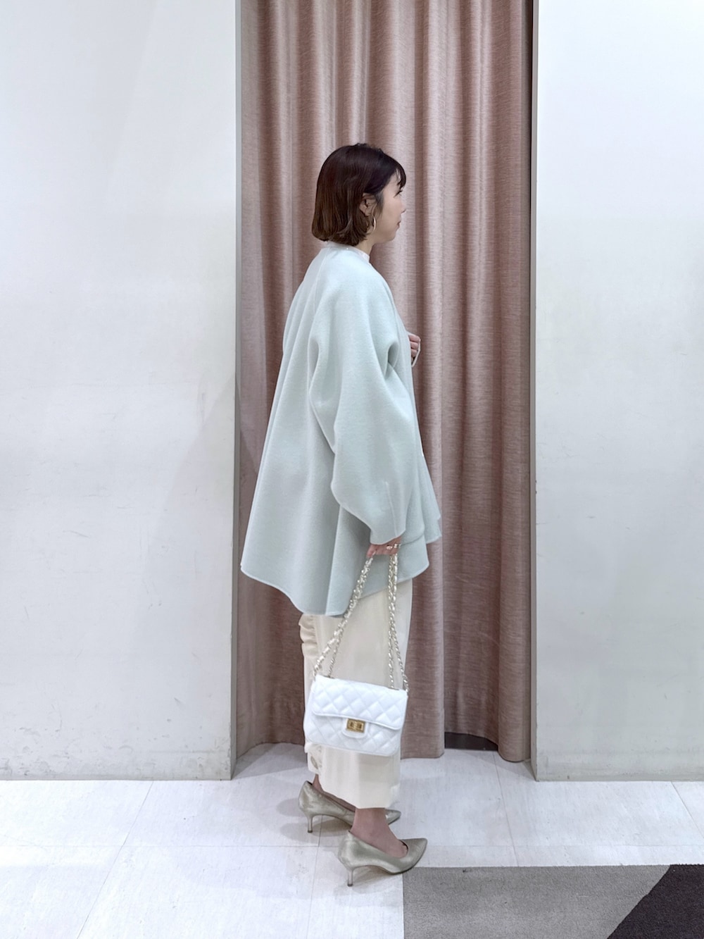 グリーン系のノーカラーコート、ホワイト系のニット/セーター、ホワイト系のキャミソールを着用したレディースの冬コーディネートの2枚目の写真