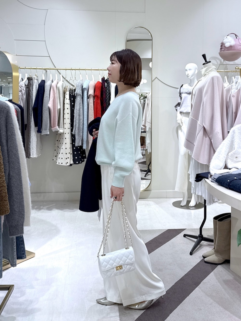 ブルー系のノーカラーコート、グリーン系のニット/セーター、ホワイト系のスラックスを着用したレディースの冬コーディネートの4枚目の写真