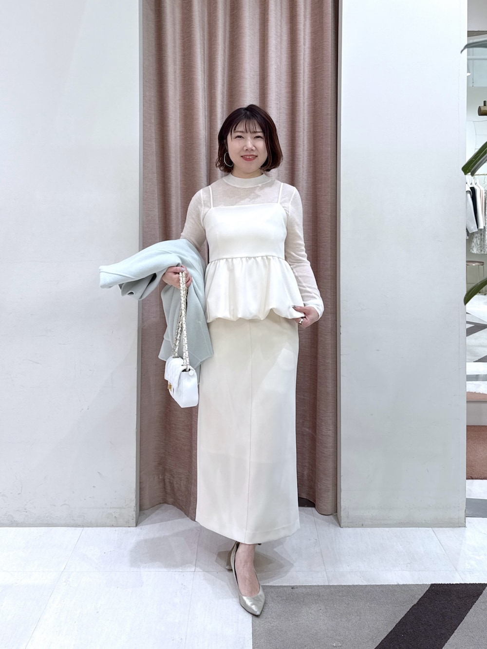 グリーン系のノーカラーコート、ホワイト系のニット/セーター、ホワイト系のキャミソールを着用したレディースの冬コーディネートの4枚目の写真