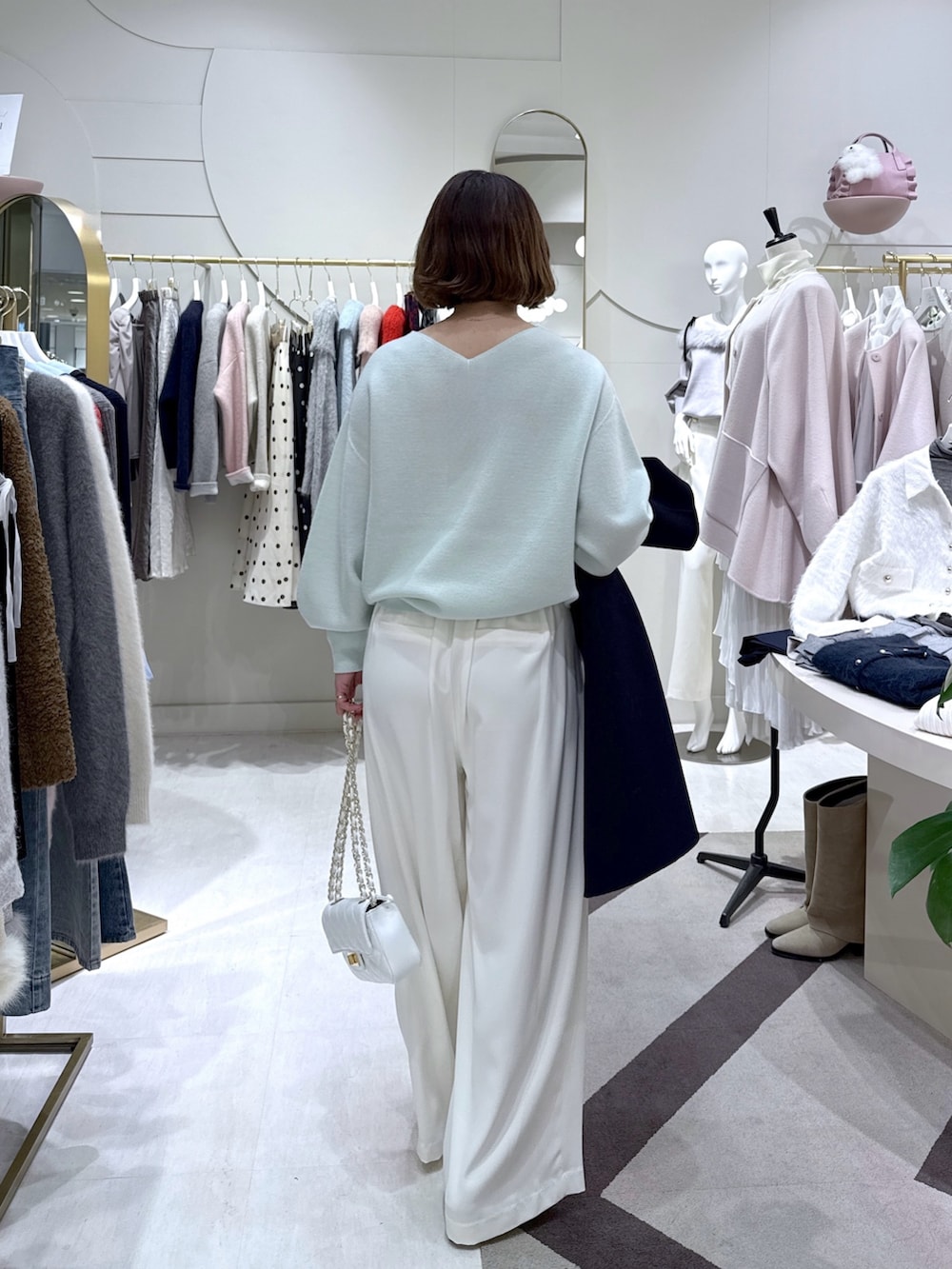 ブルー系のノーカラーコート、グリーン系のニット/セーター、ホワイト系のスラックスを着用したレディースの冬コーディネートの5枚目の写真