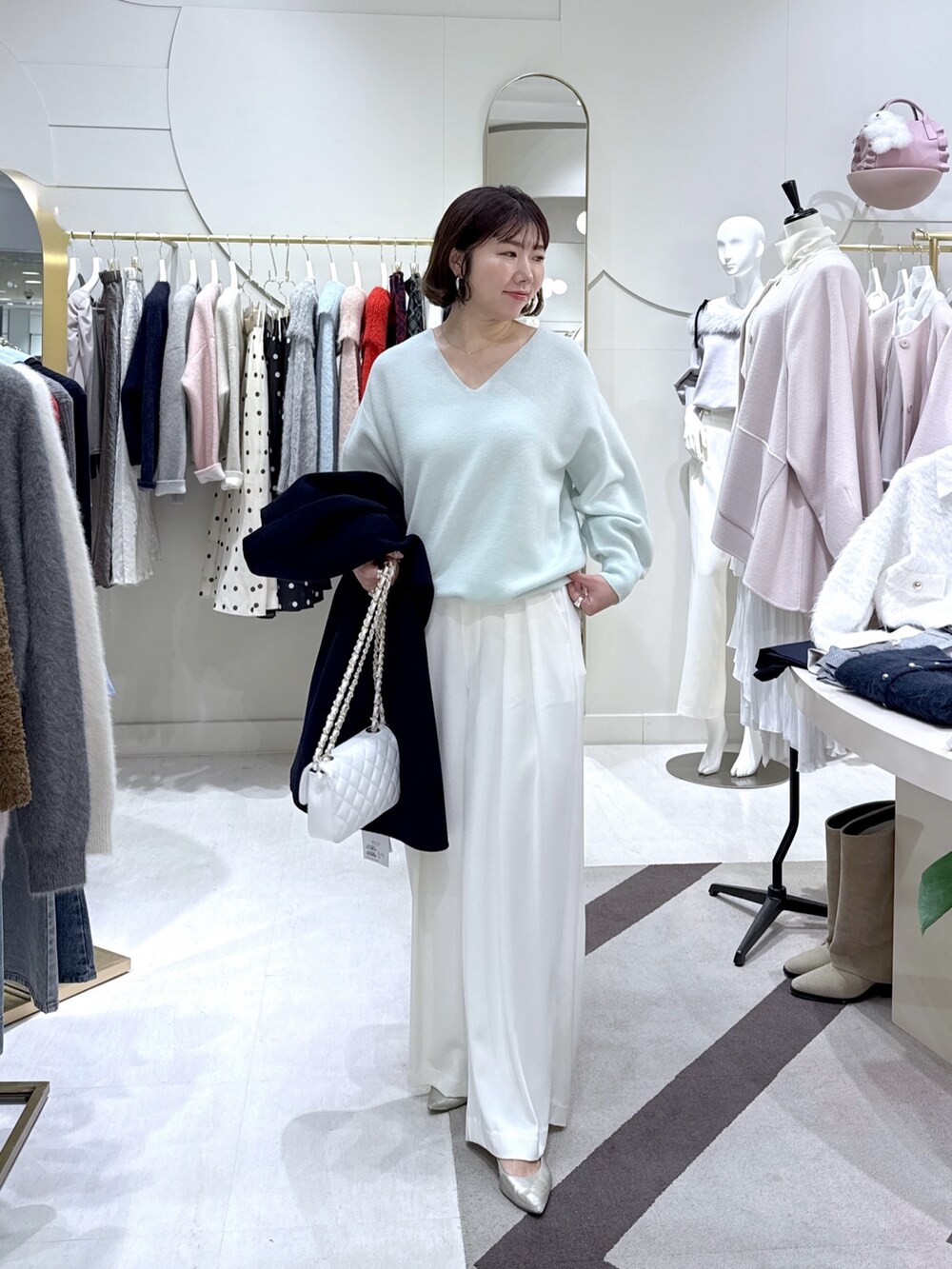 ブルー系のノーカラーコート、グリーン系のニット/セーター、ホワイト系のスラックスを着用したレディースの冬コーディネートの3枚目の写真