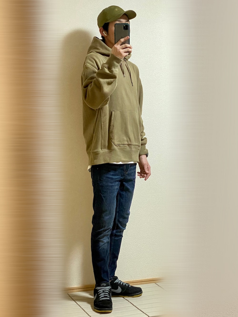 ブラック系のスニーカー、ブルー系のデニムパンツ、グリーン系のパーカーを着用したメンズの秋コーディネートの2枚目の写真