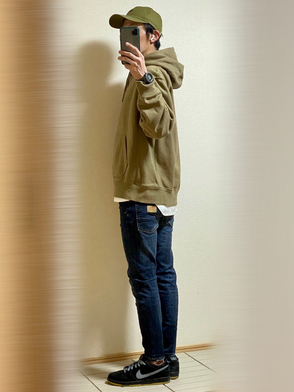 ブラック系のスニーカー、ブルー系のデニムパンツ、グリーン系のパーカーを着用したメンズの秋コーディネートの3枚目の写真