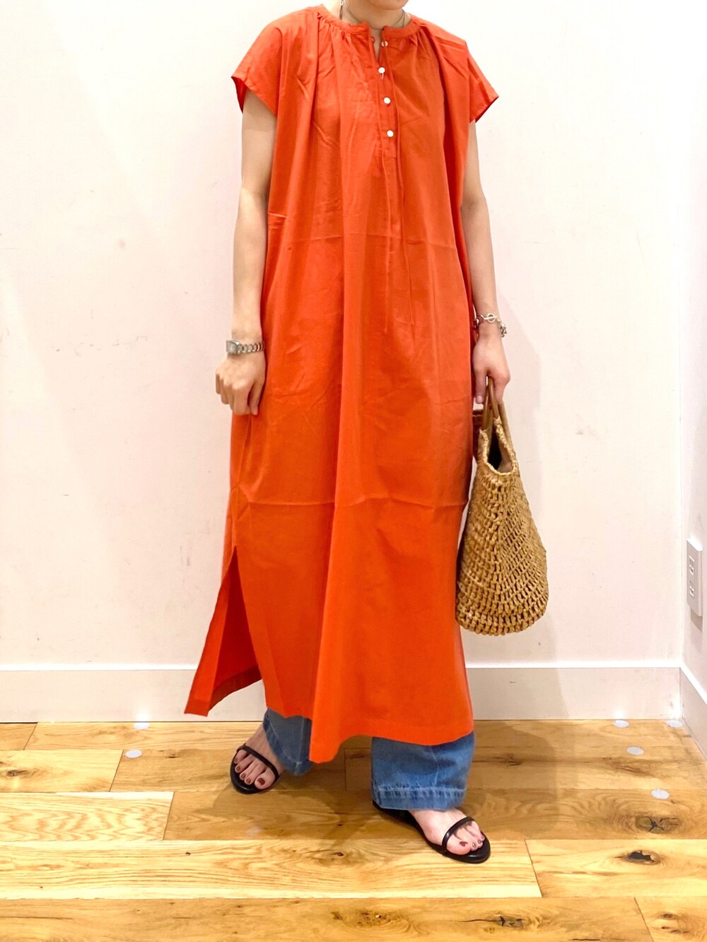 オレンジ系のワンピース、ブルー系のデニムパンツ、ベージュ系のトートバッグを着用したレディースの夏コーディネートの4枚目の写真