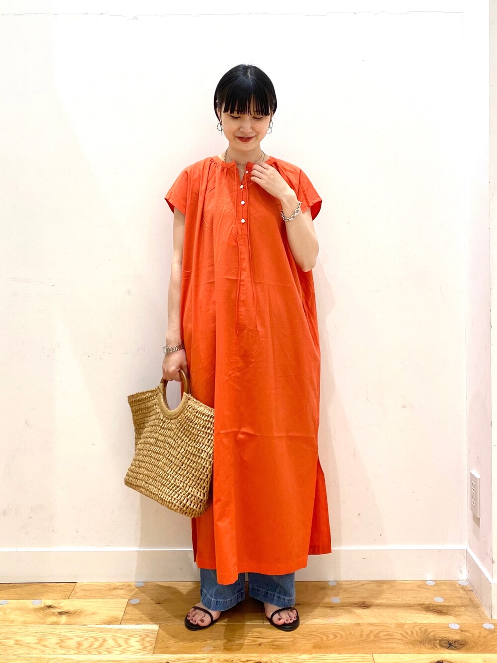 オレンジ系のワンピース、ブルー系のデニムパンツ、ベージュ系のトートバッグを着用したレディースの夏コーディネートの2枚目の写真