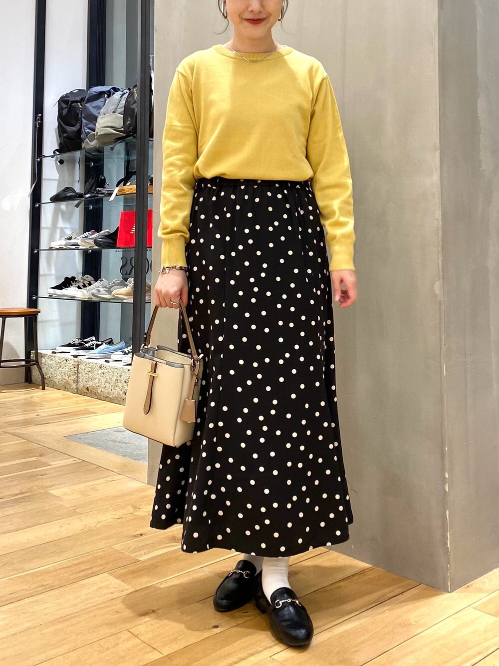 イエロー系のニット/セーター、ブラック系のスカート、ホワイト系のショルダーバッグを着用したレディースの春コーディネートの3枚目の写真