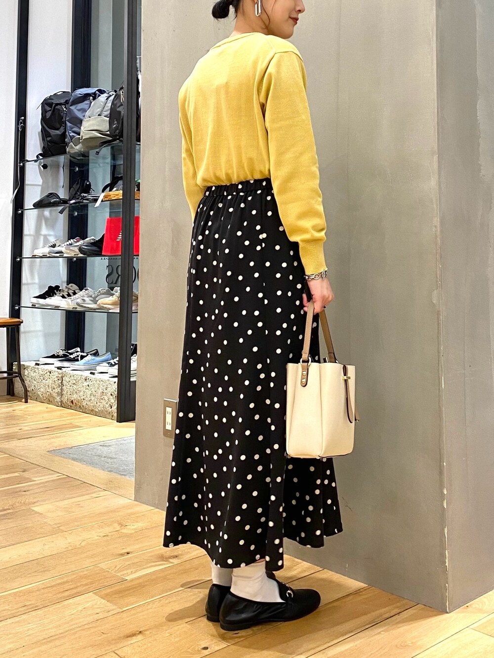 イエロー系のニット/セーター、ブラック系のスカート、ホワイト系のショルダーバッグを着用したレディースの春コーディネートの4枚目の写真
