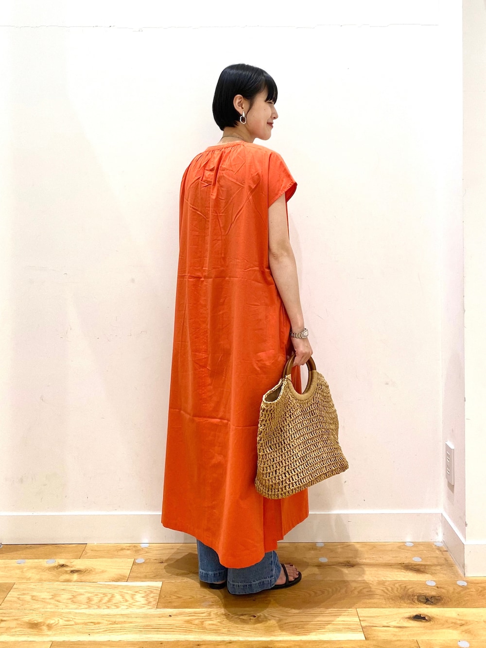 オレンジ系のワンピース、ブルー系のデニムパンツ、ベージュ系のトートバッグを着用したレディースの夏コーディネートの3枚目の写真