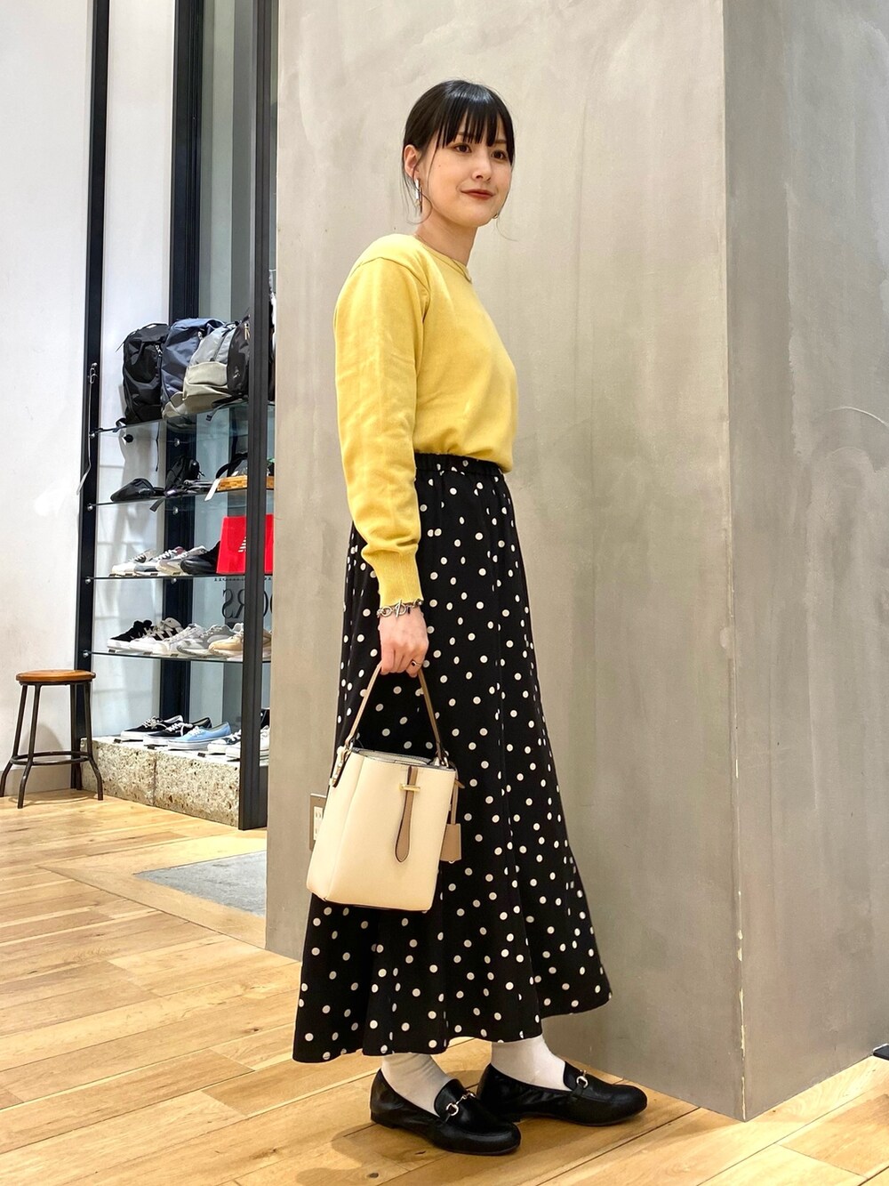 イエロー系のニット/セーター、ブラック系のスカート、ホワイト系のショルダーバッグを着用したレディースの春コーディネートの2枚目の写真