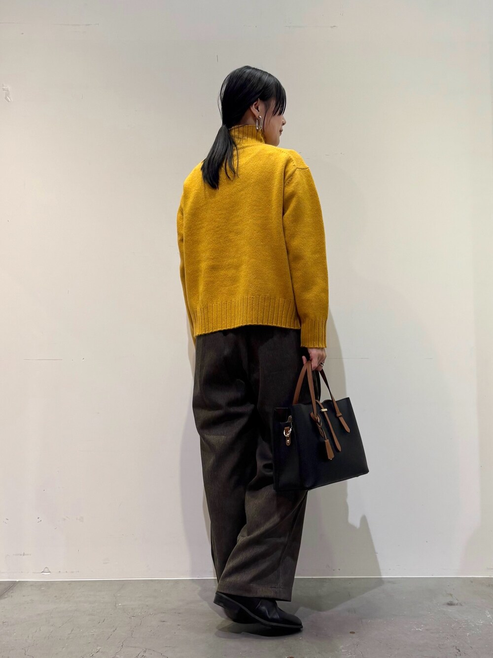 イエロー系のニット/セーター、ブラウン系のその他パンツ、ブラック系のトートバッグを着用したレディースの冬コーディネートの4枚目の写真