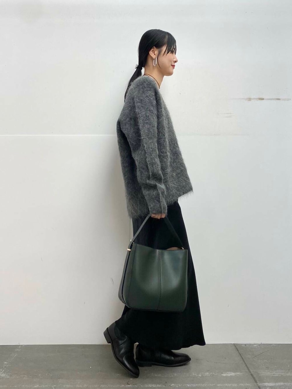 グリーン系のハンドバッグ、ブラック系のブーツ、ブラック系のスカートを着用したレディースの冬コーディネートの2枚目の写真