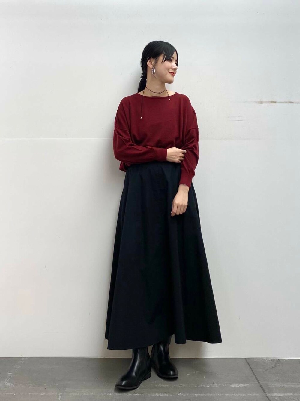 レッド系のニット/セーター、ブラック系のブーツ、ブラック系のスカートを着用したレディースの秋コーディネートの4枚目の写真