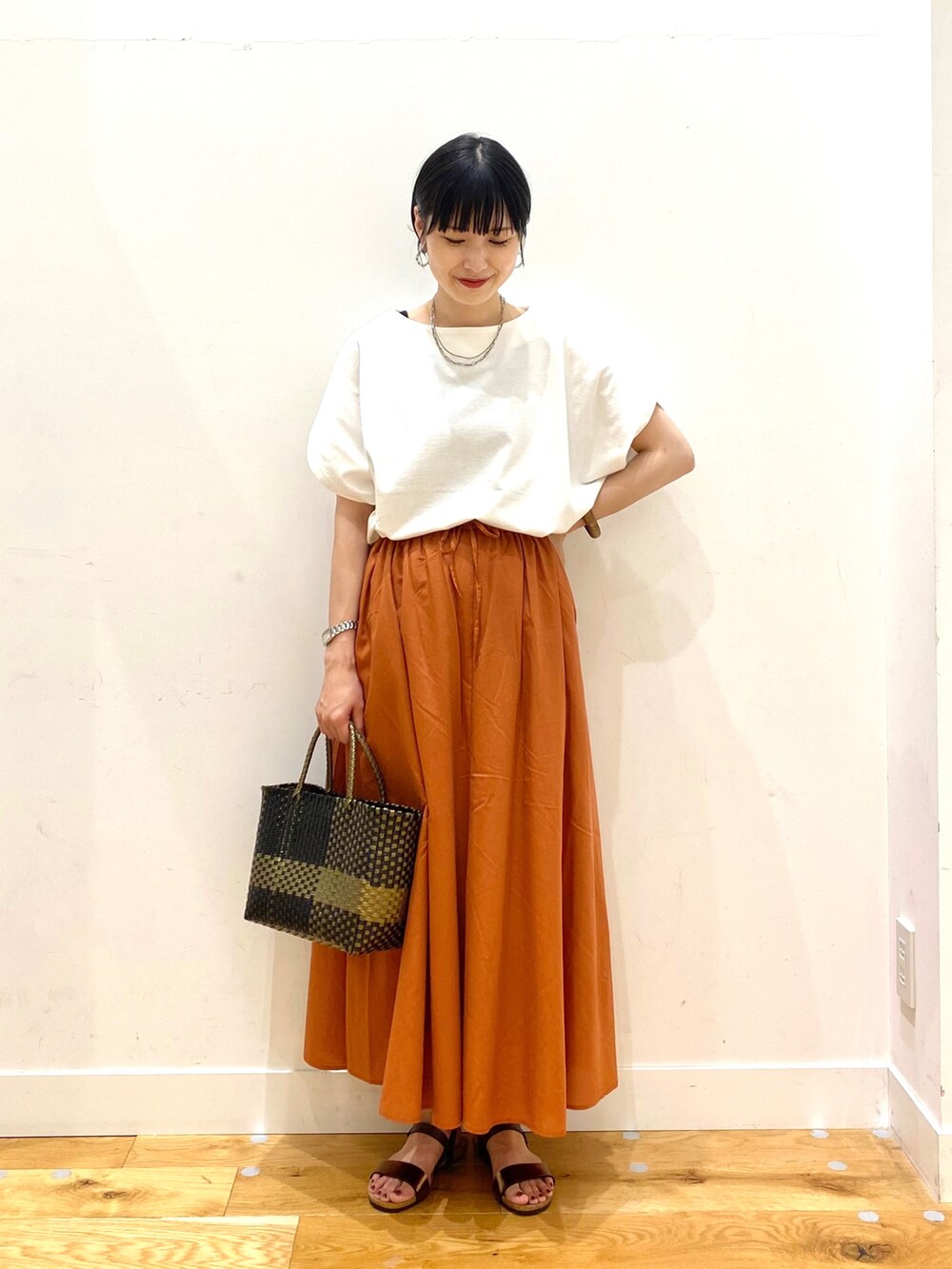 ホワイト系のTシャツ/カットソー、オレンジ系のスカート、ブラック系のトートバッグを着用したレディースの夏コーディネートの2枚目の写真