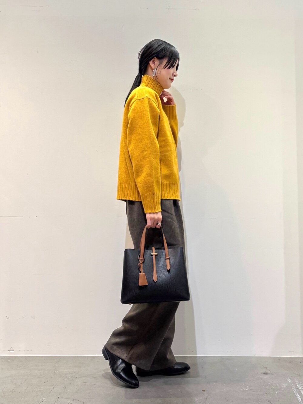 イエロー系のニット/セーター、ブラウン系のその他パンツ、ブラック系のトートバッグを着用したレディースの冬コーディネートの2枚目の写真