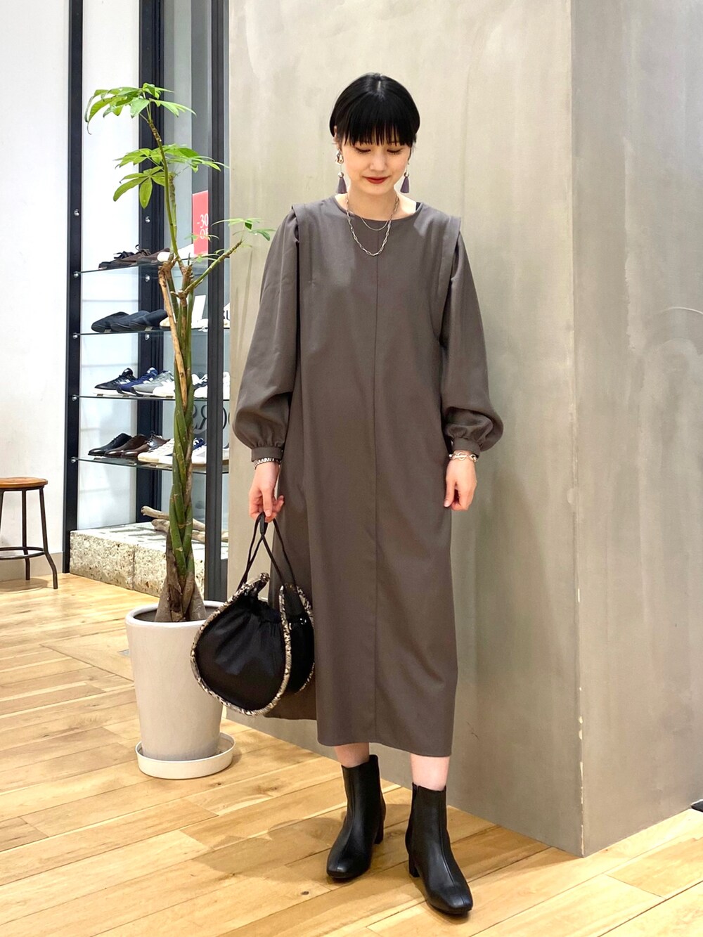 グレー系のワンピース、ブラック系のショルダーバッグ、ブラック系のブーツを着用したレディースの冬コーディネートの3枚目の写真
