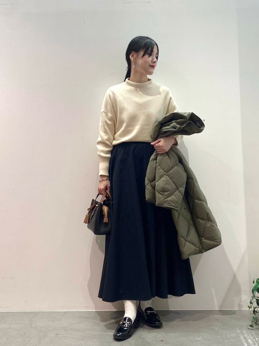 ブラック系のハンドバッグ、グリーン系のダウンジャケット/コート、ブラック系のローファーを着用したレディースの秋コーディネートの4枚目の写真