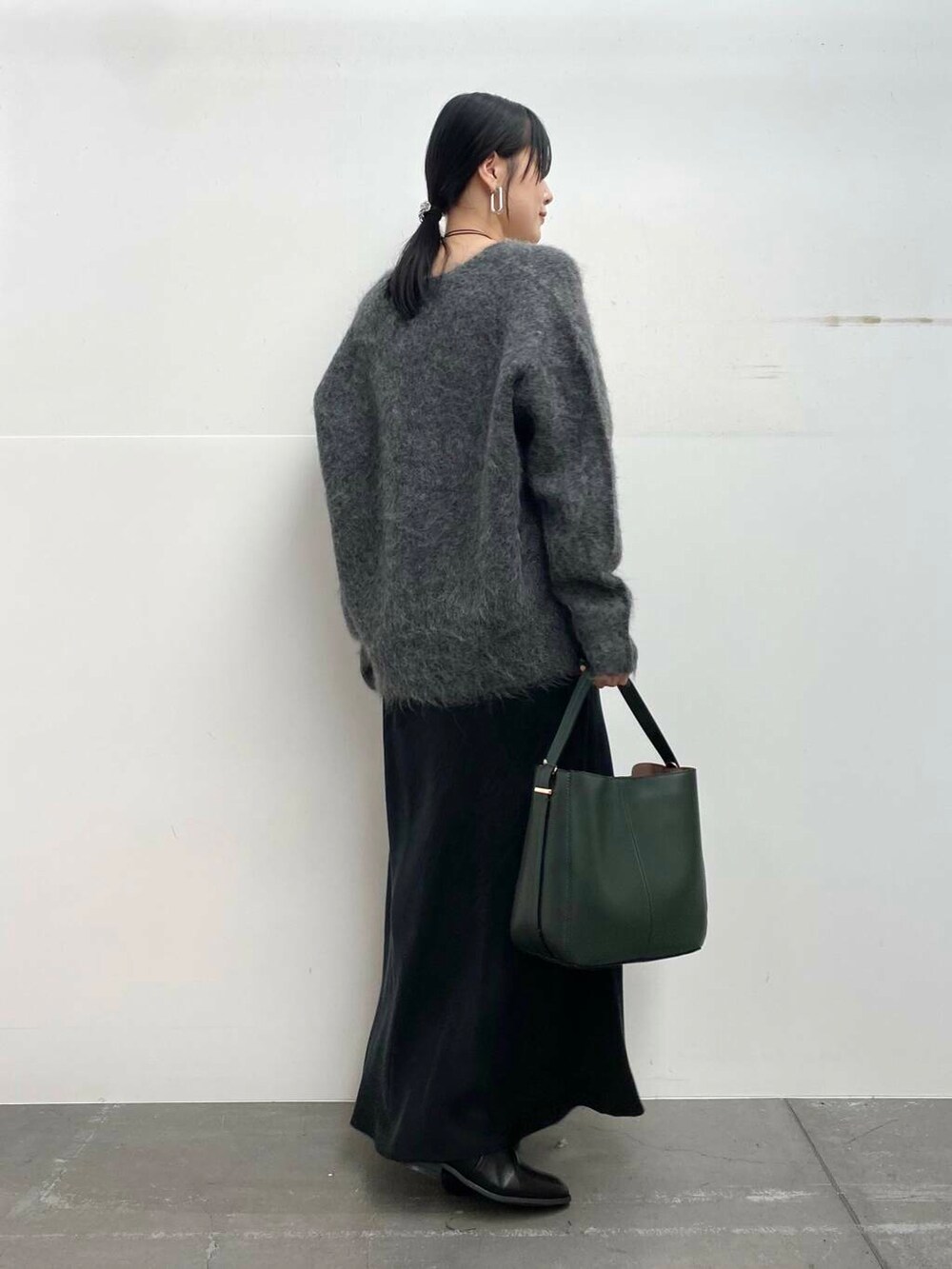 グリーン系のハンドバッグ、ブラック系のブーツ、ブラック系のスカートを着用したレディースの冬コーディネートの4枚目の写真