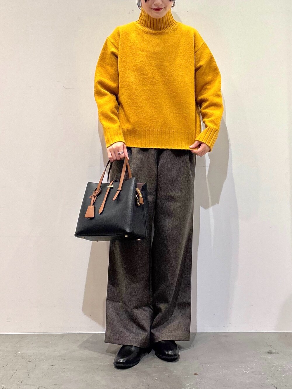 イエロー系のニット/セーター、ブラウン系のその他パンツ、ブラック系のトートバッグを着用したレディースの冬コーディネートの5枚目の写真