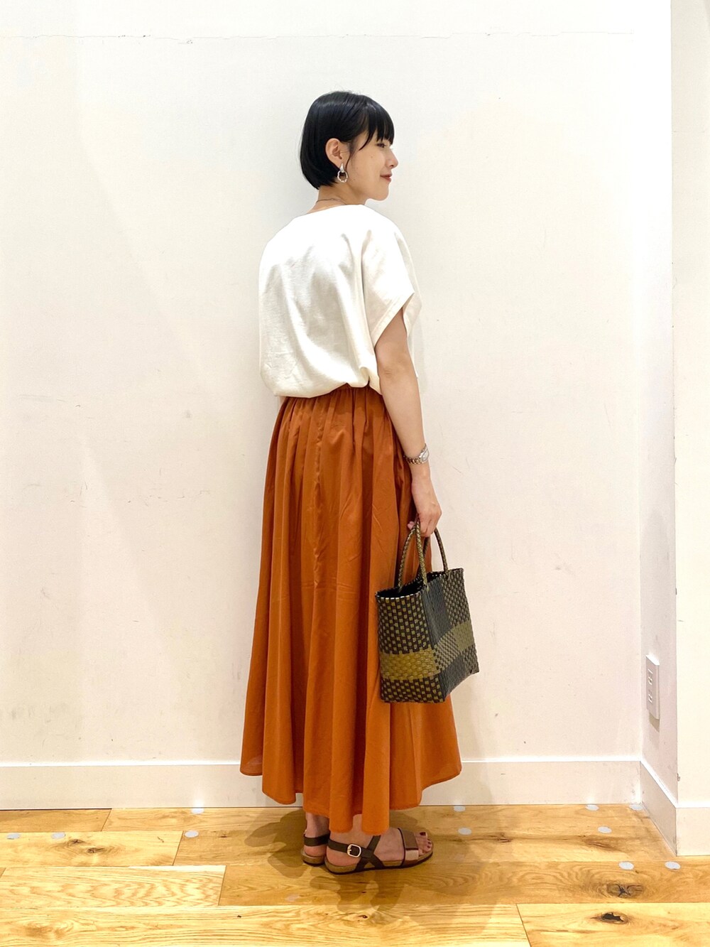 ホワイト系のTシャツ/カットソー、オレンジ系のスカート、ブラック系のトートバッグを着用したレディースの夏コーディネートの3枚目の写真