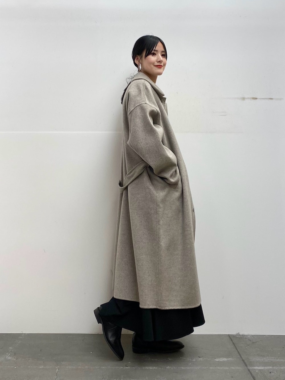 グレー系のステンカラーコート、レッド系のニット/セーター、ブラック系のスカートを着用したレディースの秋コーディネートの2枚目の写真