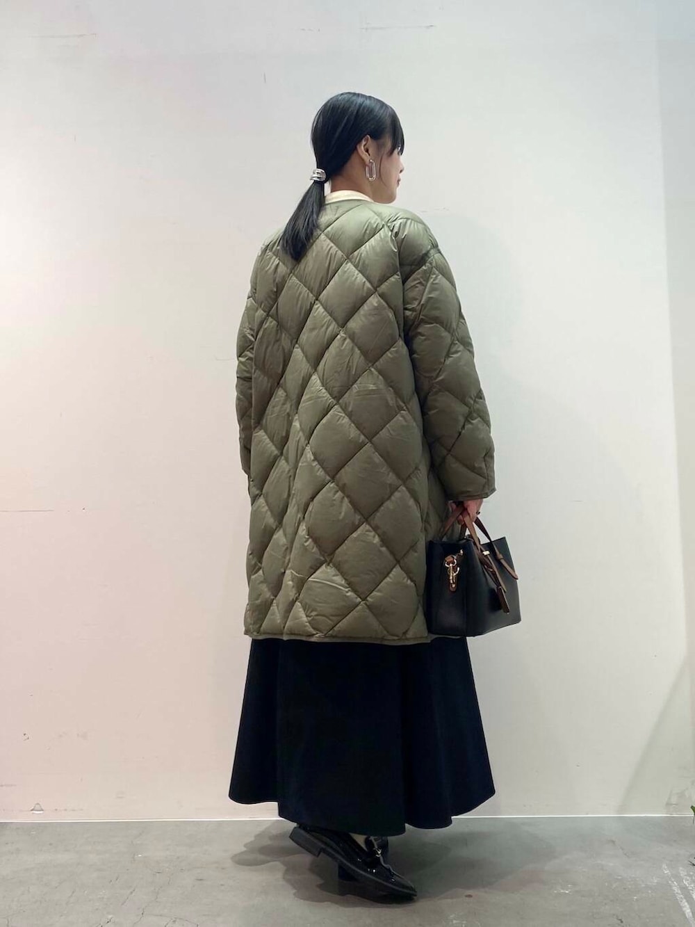 ブラック系のハンドバッグ、グリーン系のダウンジャケット/コート、ブラック系のローファーを着用したレディースの秋コーディネートの3枚目の写真