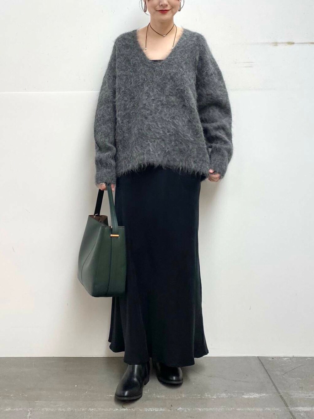 グリーン系のハンドバッグ、ブラック系のブーツ、ブラック系のスカートを着用したレディースの冬コーディネートの5枚目の写真