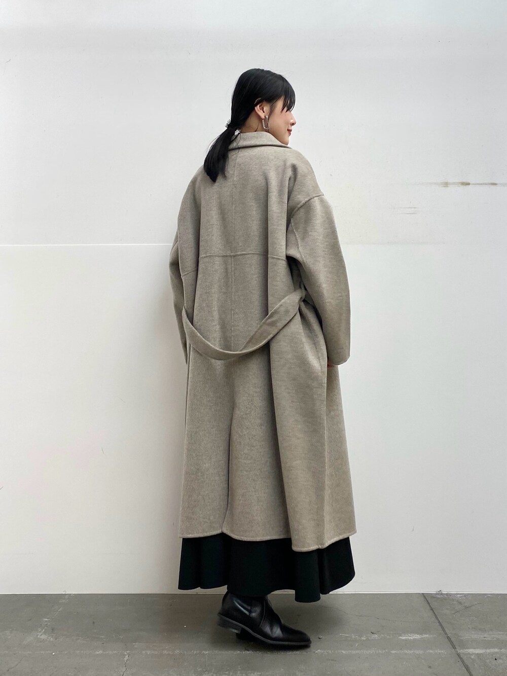 グレー系のステンカラーコート、レッド系のニット/セーター、ブラック系のスカートを着用したレディースの秋コーディネートの3枚目の写真